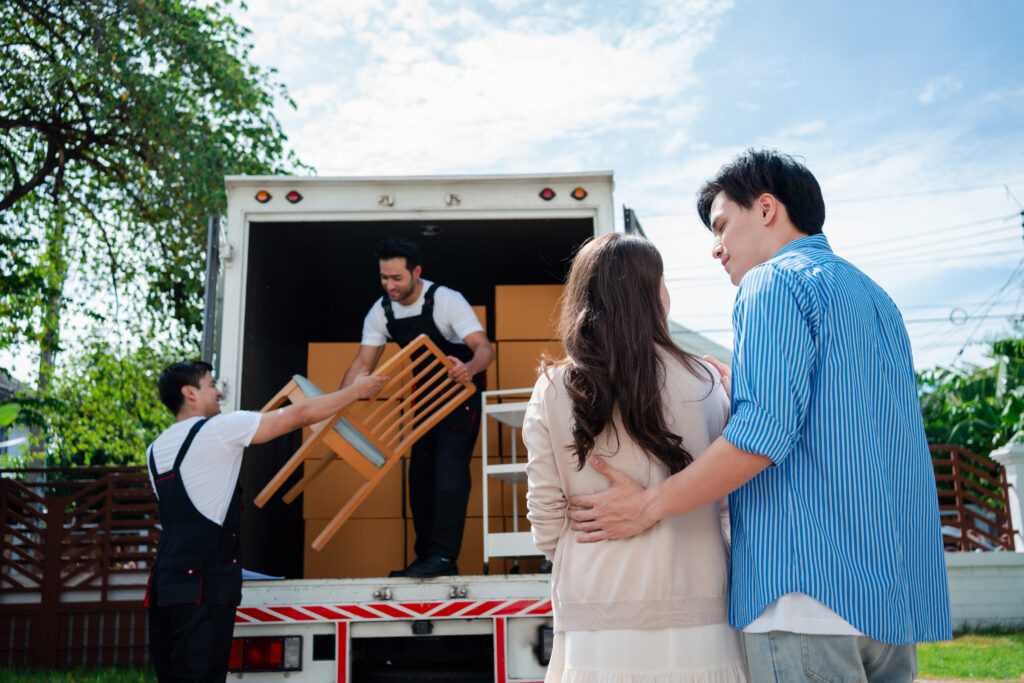 asian couple check while unloading boxes and furniture from a pickup truck to a new house with service cargo two men movers worker in uniform lifting boxes. concept of home moving and delivery.